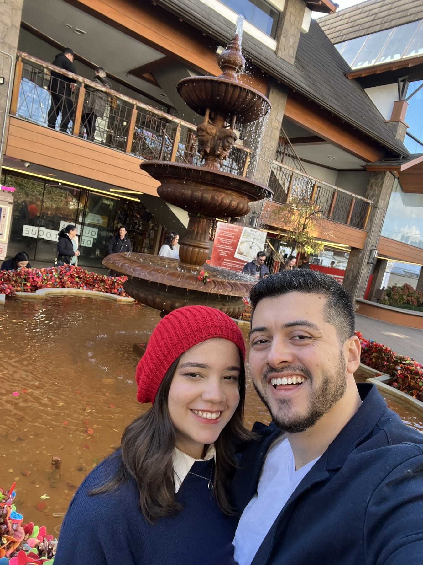 Leandro e Paolla sorrindo em frente a uma fonte
